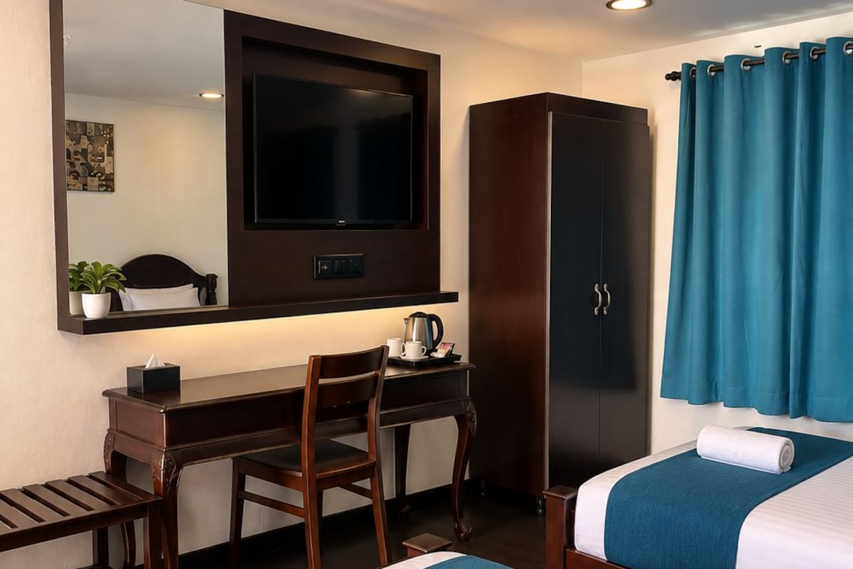 A hotel room with two beds, a desk, a television, a wardrobe, and a bathroom with a shower curtain.