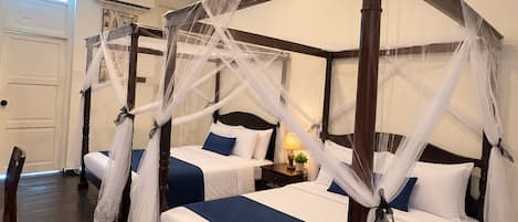 A four-poster bed with white and blue bedding, a ceiling fan, and a nightstand with a lamp and a plant.