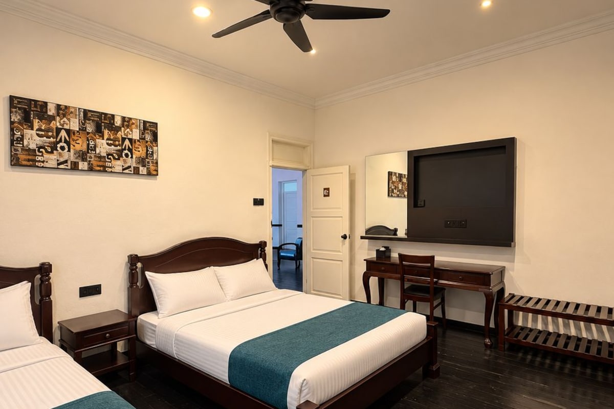 A hotel room with two beds, a ceiling fan, a TV, and a door leading to a bathroom.