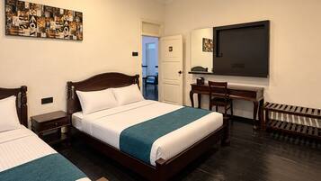 A hotel room with two beds, a ceiling fan, a TV, and a door leading to a bathroom.