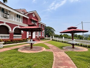 A red building with a white balcony, two red umbrellas, and a well-maintained lawn.