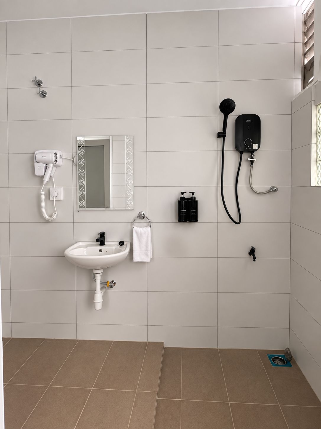 A bathroom with a white sink, a handheld hair dryer, a handheld showerhead, and a mirror with a decorative frame.