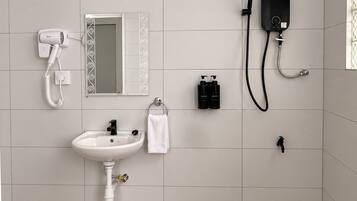 A bathroom with a white sink, a handheld hair dryer, a handheld showerhead, and a mirror with a decorative frame.