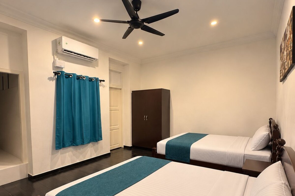 A hotel room with two beds, a ceiling fan, an air conditioning unit, and a wardrobe.