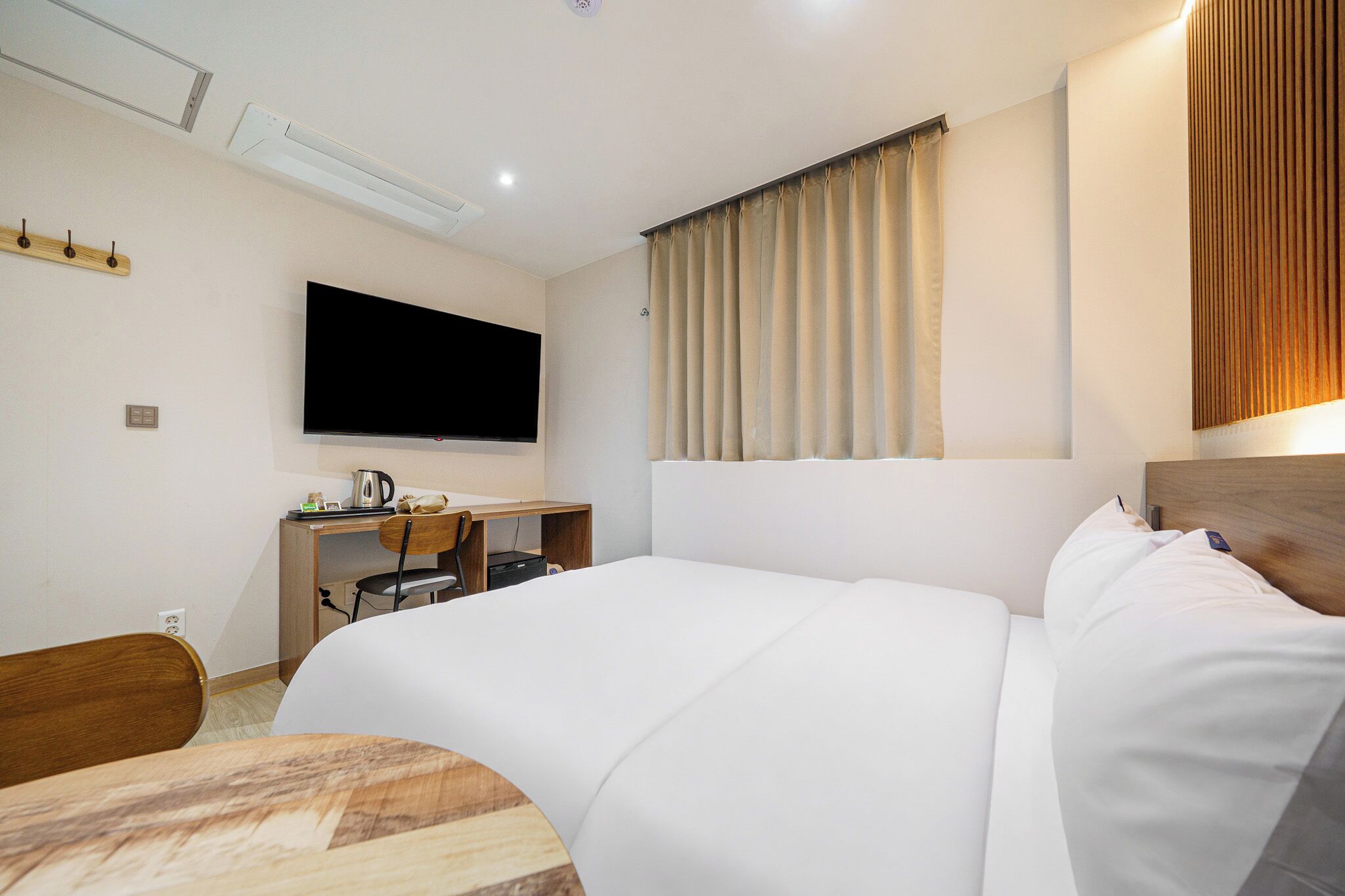 Habitació d'hotel amb un llit, escriptori, cadira, televisió i finestra amb cortines.