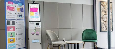 A kiosk with a touchscreen interface, a chair, a table, and a decorative wall panel.