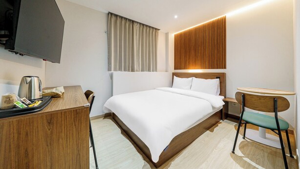 A hotel room with a bed, a desk, a chair, a TV, and a window with curtains.