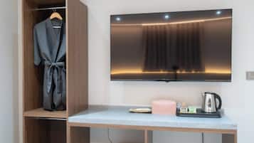 A room with a wooden wardrobe, a flat-screen TV mounted on the wall, a small table with a kettle and a pink candle.