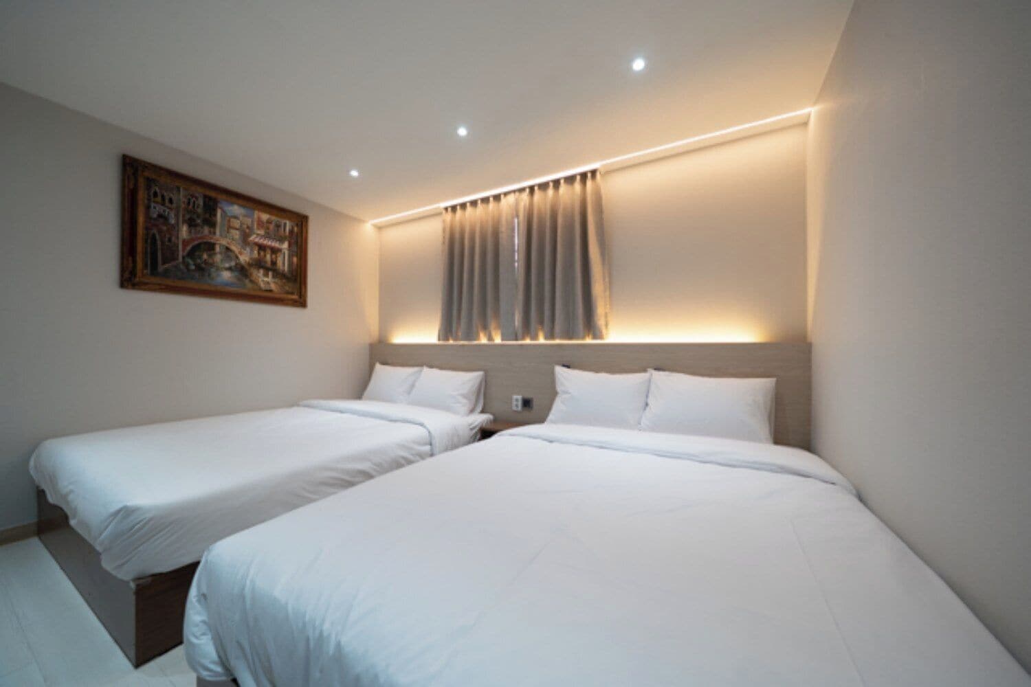 A hotel room with two single beds, a painting on the wall, and a window with curtains.