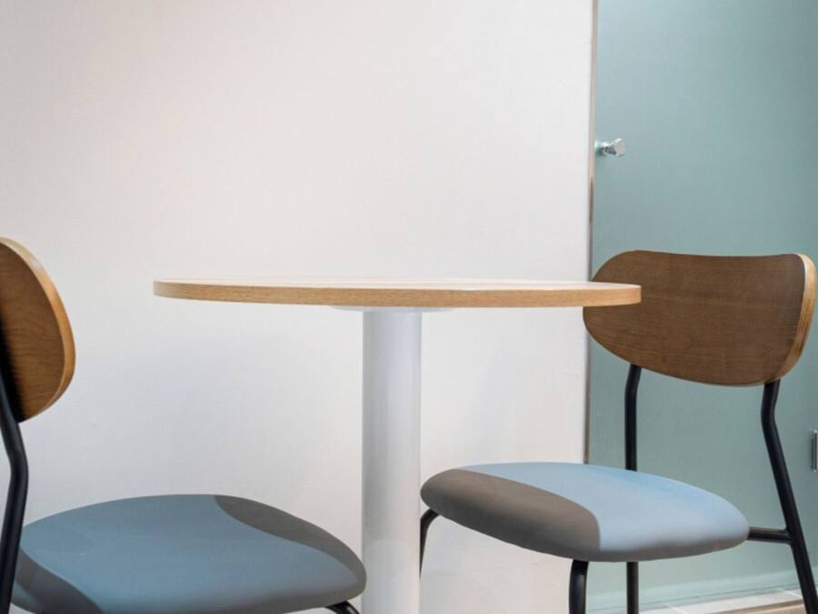 A small table with two chairs, one with a wooden back and seat, and the other with a grey upholstered seat.