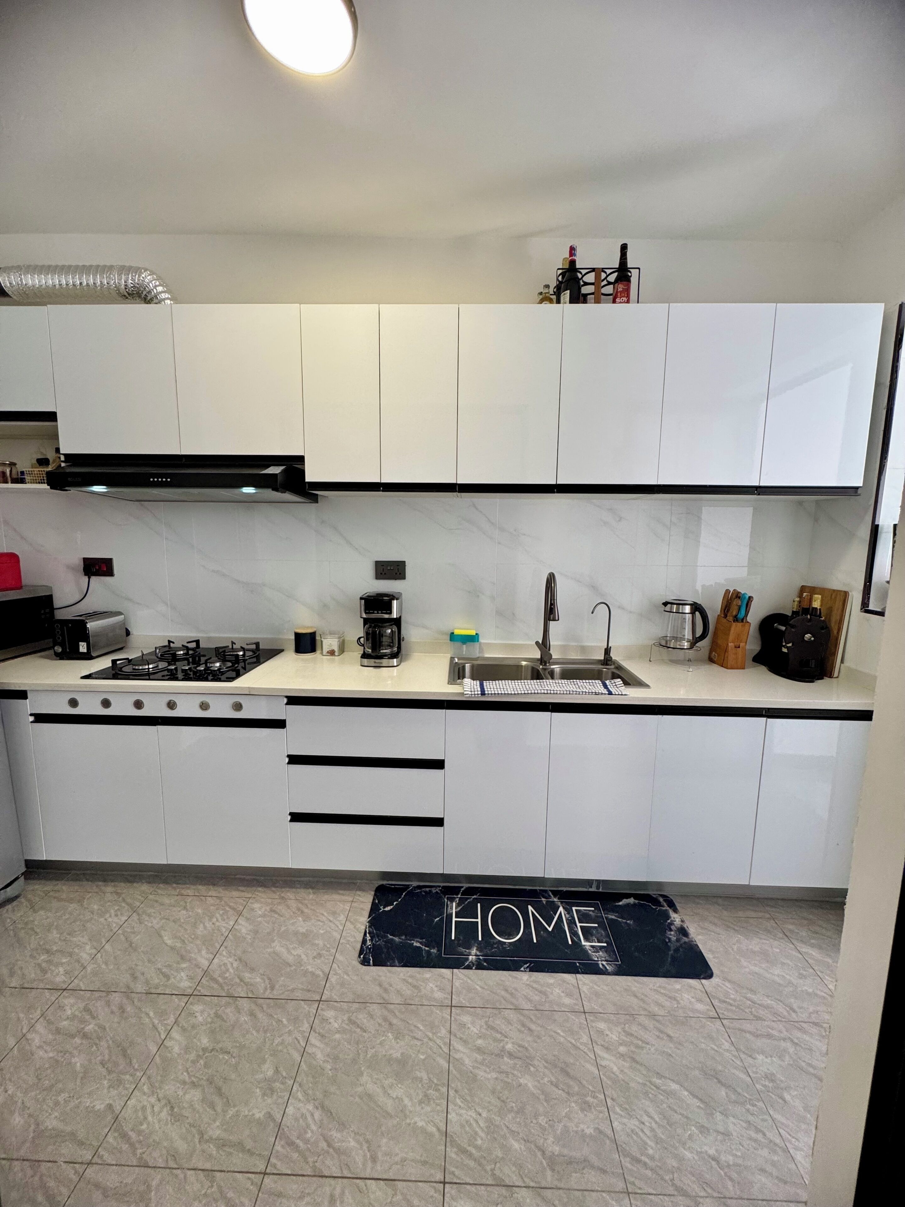 Une cuisine moderne avec des meubles blancs, une cuisinière à gaz, une machine à café et un évier.