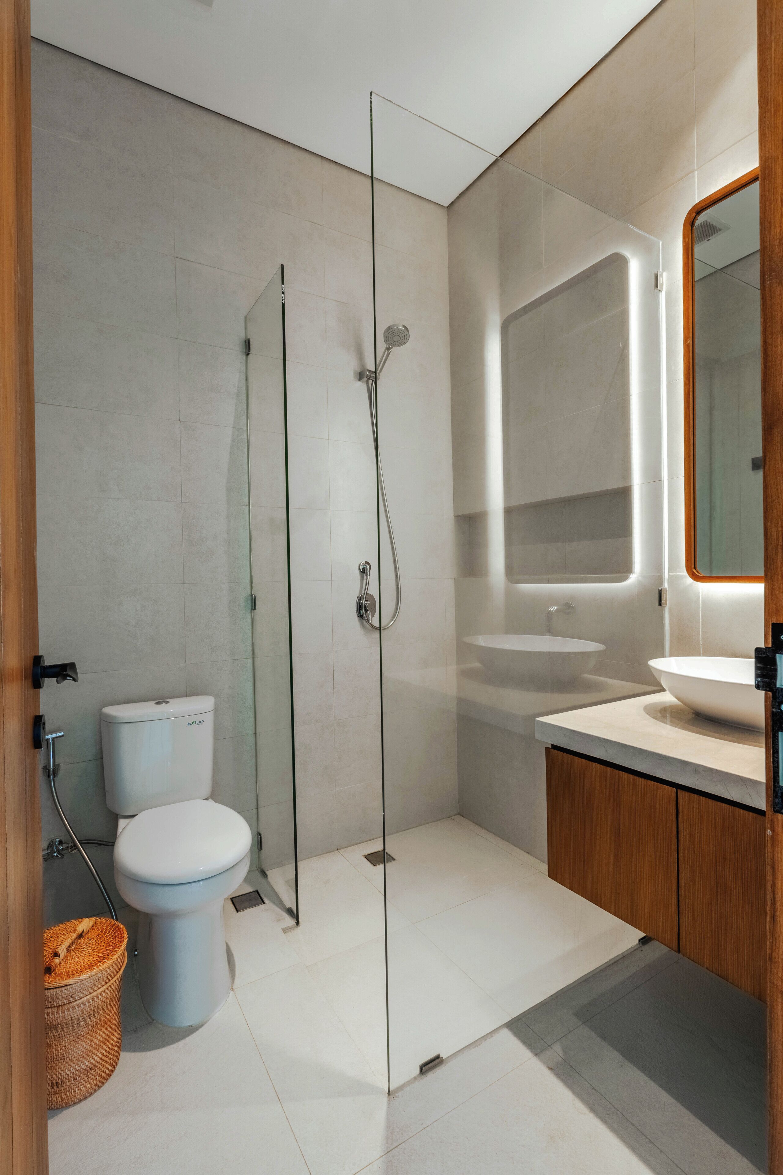 Un baño moderno con cabina de ducha de vidrio, inodoro, lavamanos y mueble de madera.