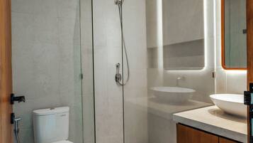 Un baño moderno con cabina de ducha de vidrio, inodoro, lavamanos y mueble de madera.