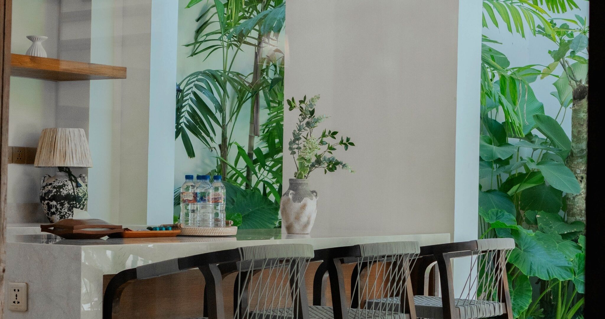 A modern kitchen with a bar area, featuring a large window with a view of tropical plants.