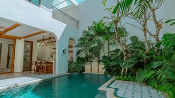 Un área de piscina interior moderna con comedor y una escalera que conduce a un nivel superior.
