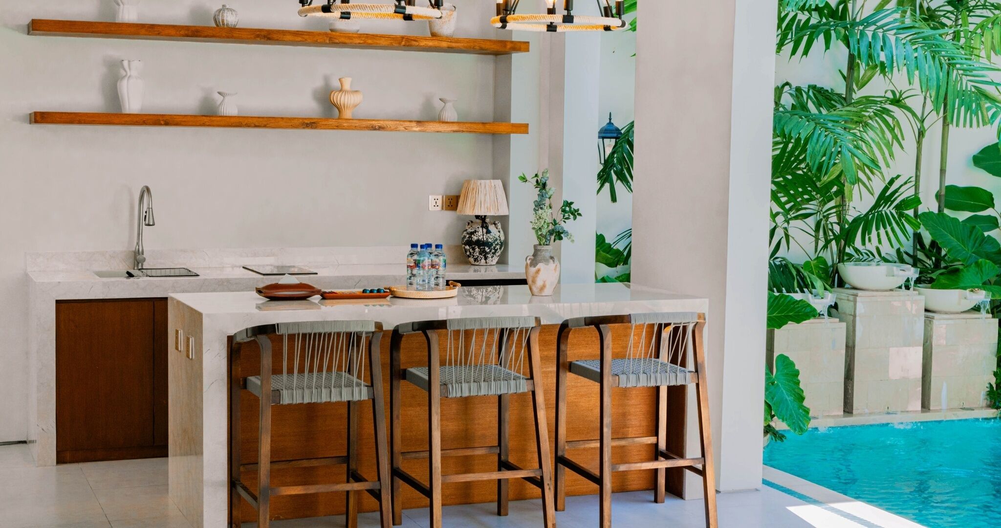 Una cocina moderna con barra, estantes de madera y vista a la piscina.