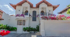 A two-story building with a white facade, multiple windows, and balconies adorned with flowering plants. - Uma Mimpi by Navya (Badung)