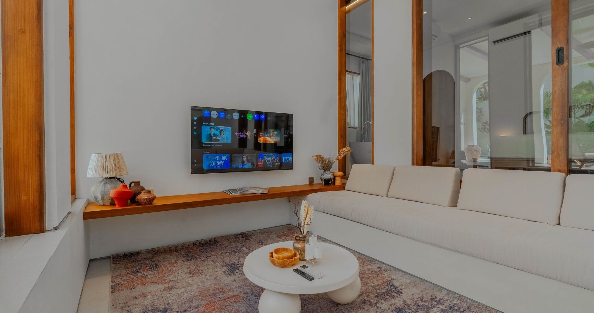 Ein modernes Wohnzimmer mit einem flachbildfernseher an der Wand, einem weißen Sofa, einem runden Couchtisch und einer dekorativen Vase.