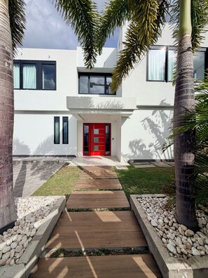 A modern two-story building with a red door, a stone pathway leading to the entrance, and a well-maintained lawn.