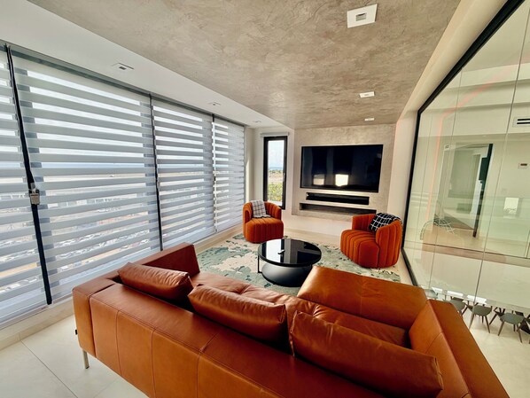 A modern living room with a leather sofa, a glass coffee table, and a flat-screen TV mounted on the wall.