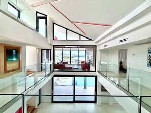 Un interior moderno con barandilla de vidrio, una zona de estar con vistas y una escalera.