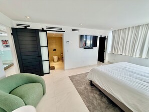 Moderni hotellihuone, jossa on sänky, vihreä tuoli, televisio ja kylpyhuone.