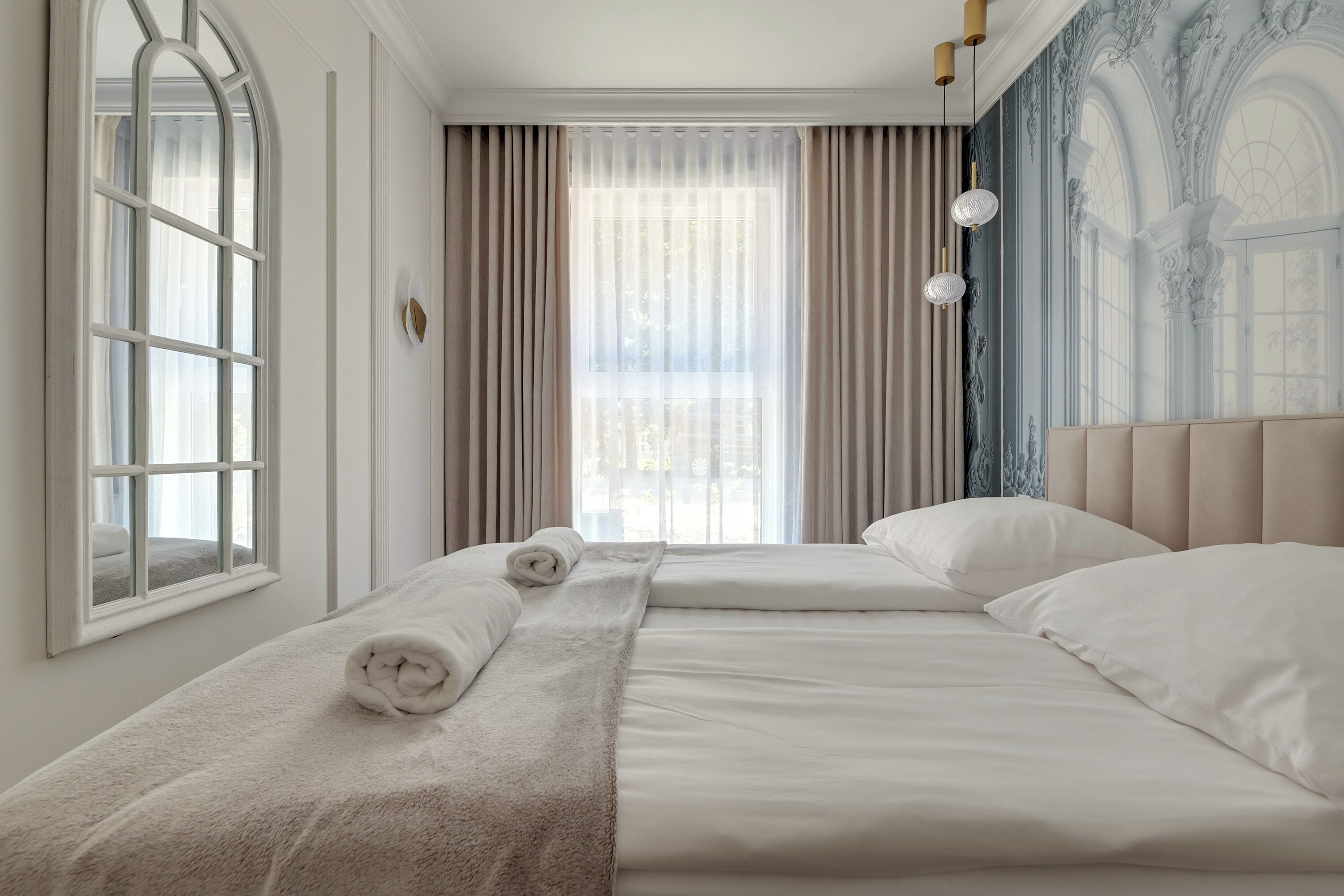 A hotel room with a large bed, a window with curtains, and a decorative wall.