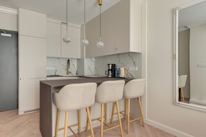 A modern kitchen with a marble countertop, a coffee maker, and three bar stools. - Mostek 2137 by Grand Apartments (Gdańsk)