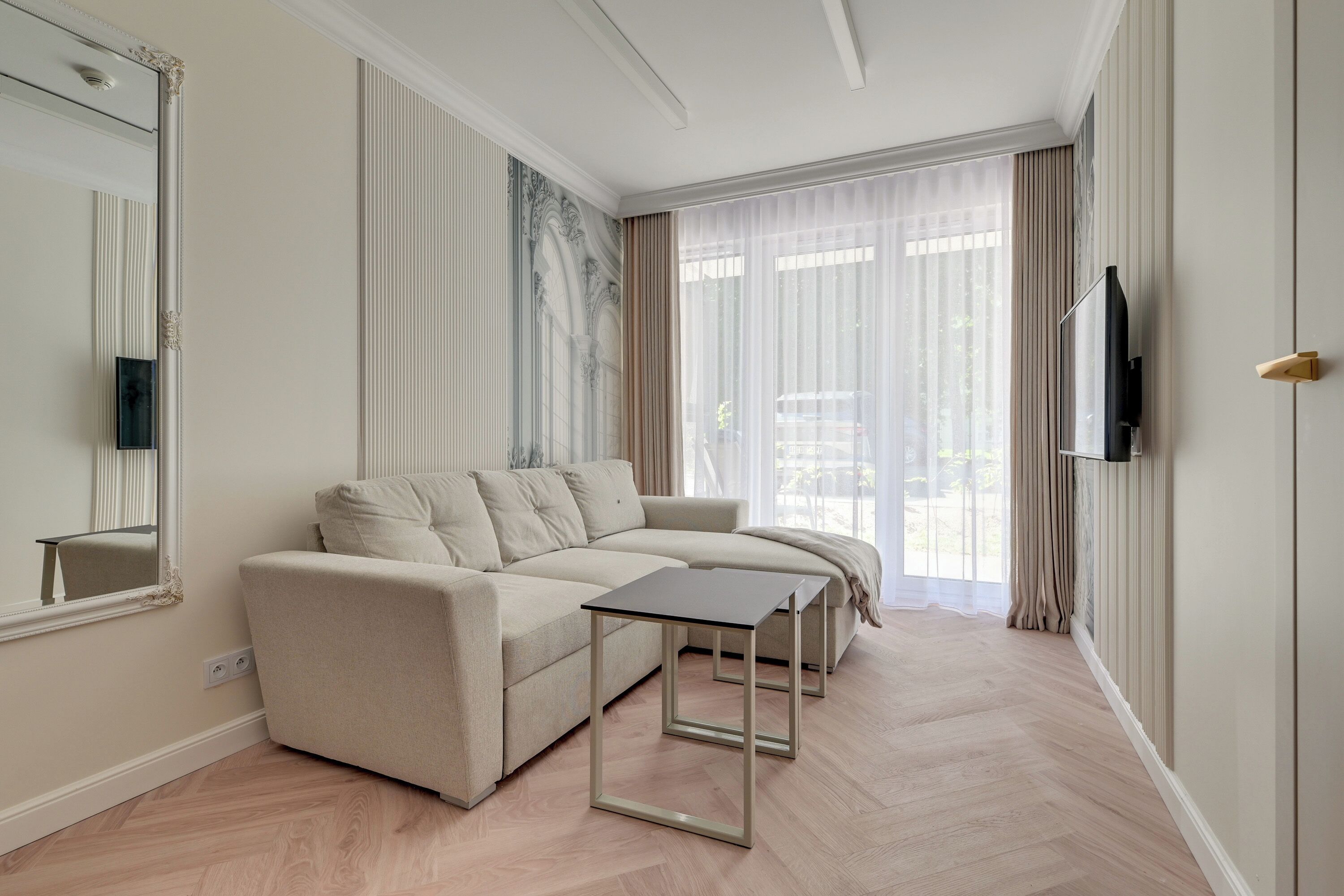 Un salon moderne avec un canapé, une table basse, un téléviseur à écran plat et une grande fenêtre avec des rideaux.