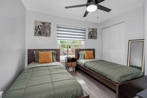 Ein Schlafzimmer mit zwei Betten, einem Deckenventilator, einem Fenster mit Jalousien und Bildern an den Wänden.