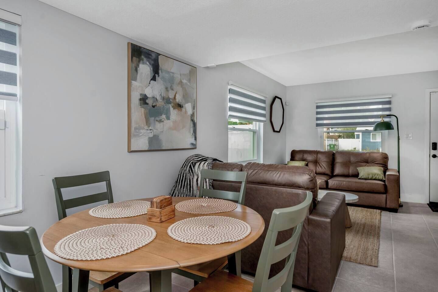 Una sala de estar moderna con un sofá de cuero marrón, una mesa de comedor con individuales y un cuadro abstracto grande en la pared.