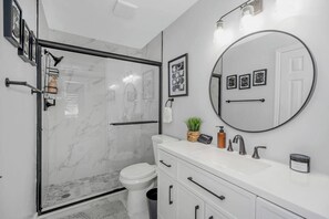Een moderne badkamer met een glazen douchecabine, een wit toilet, een wastafel met spiegel en een kleine plant in pot.