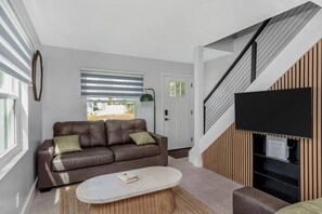 Un salon moderne avec un canapé en cuir, une table basse ronde et un téléviseur à écran plat fixé à un mur en bois.