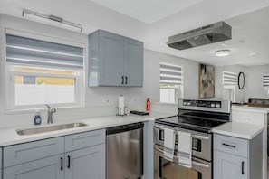 Une cuisine moderne dotée d’appareils électroménagers en acier inoxydable, de meubles de rangement gris et d’une fenêtre avec des stores.