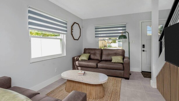 Ein Wohnzimmer mit einem braunen Ledersofa, einem runden Couchtisch und einem großen Fenster mit Jalousien.
