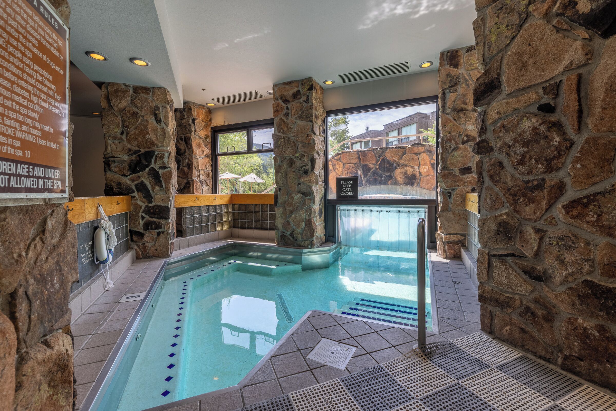An indoor swimming pool with stone walls and a view of a building outside.