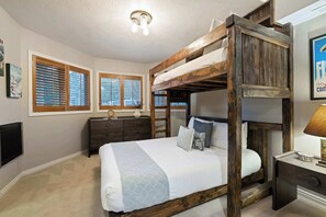 Ein Schlafzimmer mit Etagenbett, Kommode, Nachttisch und an der Wand montiertem Fernseher.