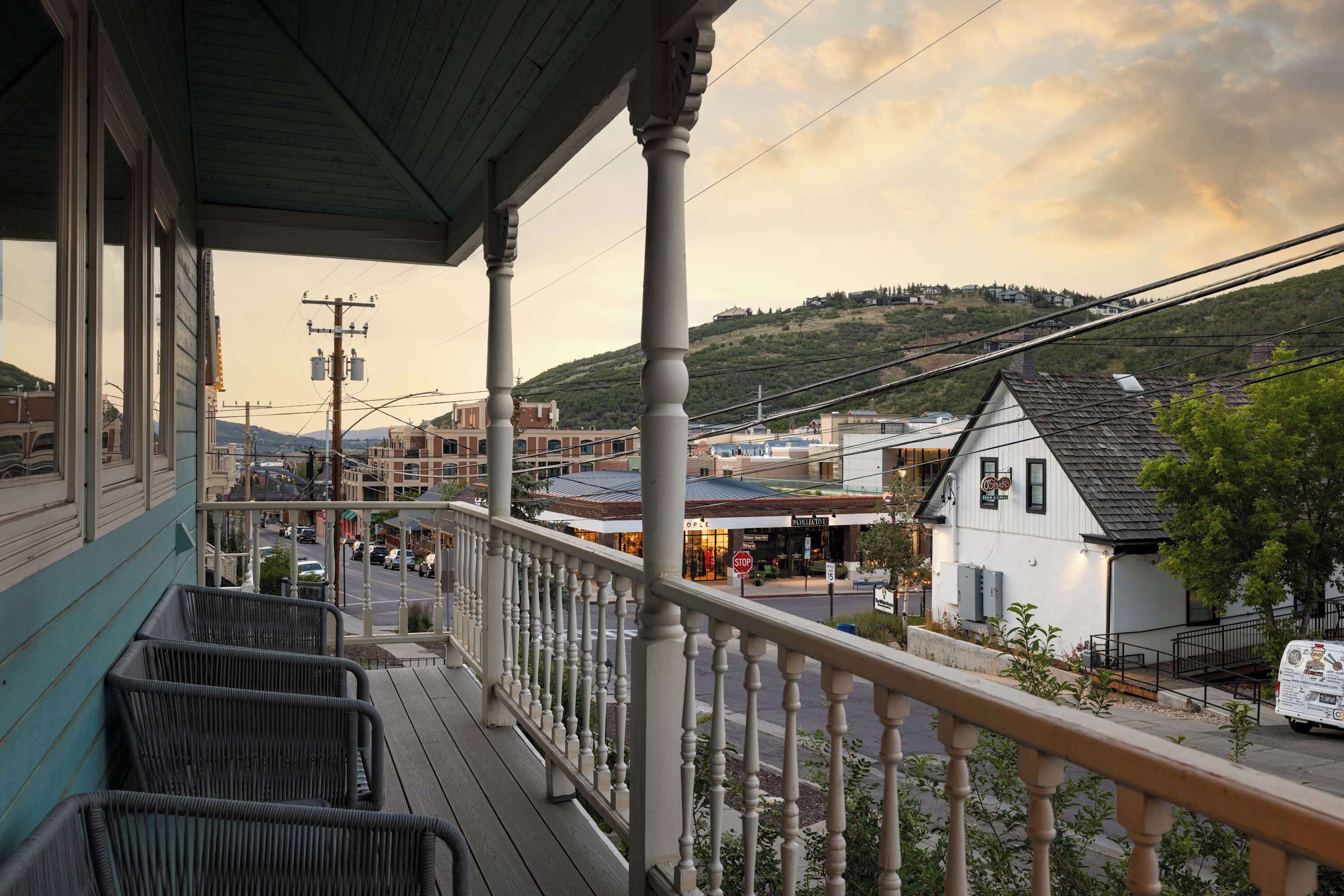 A porch with wicker furniture, overlooking a street with buildings and a hill in the background.