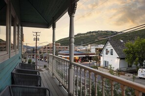 Eine Veranda mit Korbmöbeln, mit Blick auf eine Straße mit Gebäuden und einer Hügelkulisse im Hintergrund.