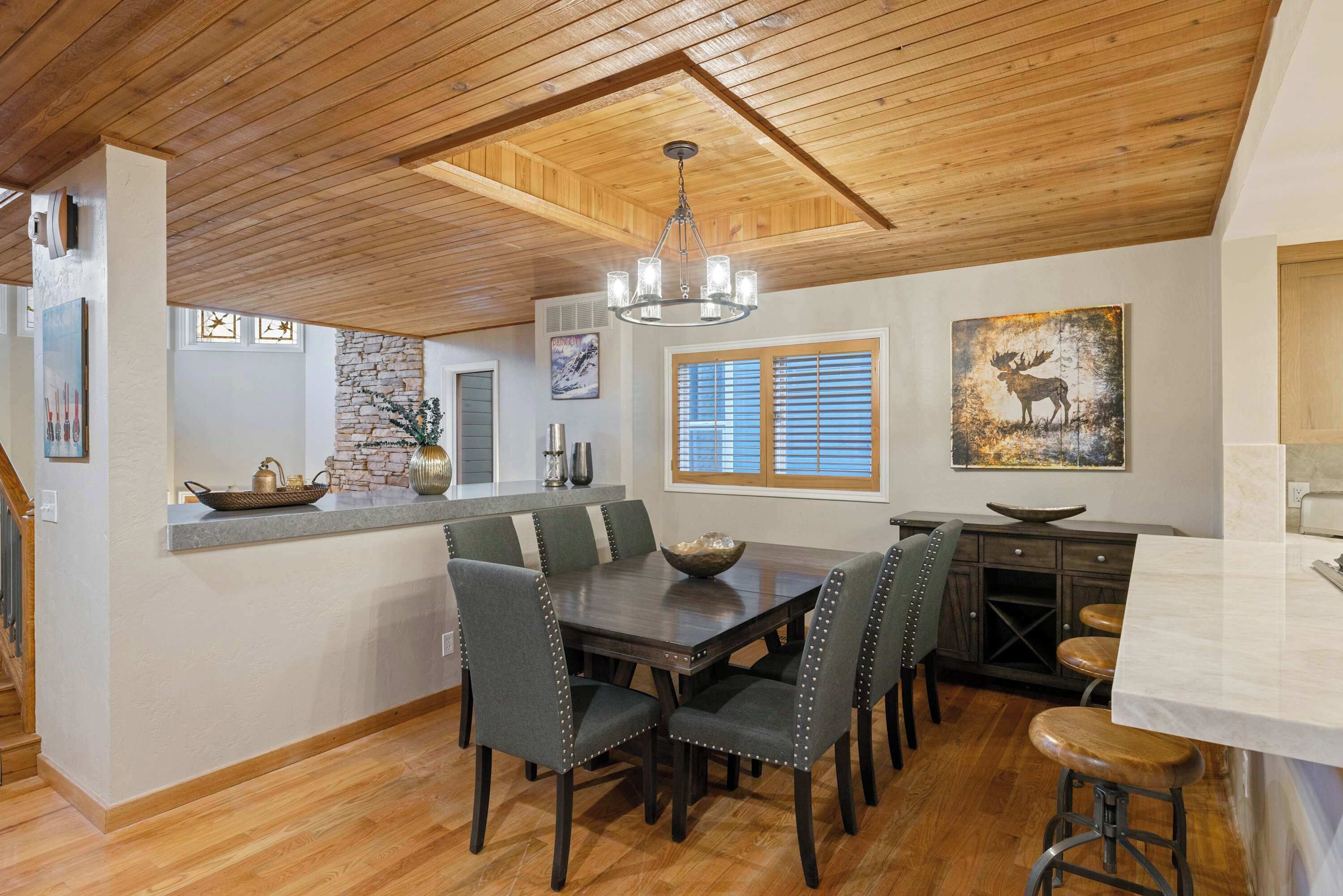 A spacious kitchen with a central island, wooden ceiling, and a dining area with chairs and a table.