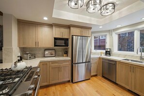 Eine moderne Küche mit Holdekor, Edelstahlgeräten, einem Gasherd und einem Fenster mit Blick auf Bäume.