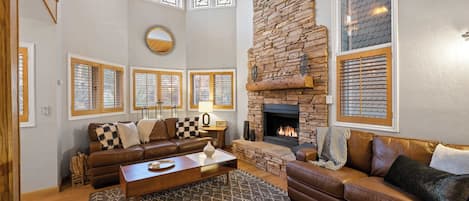 Amplia sala de estar con chimenea de piedra, sofás de cuero y un ventanal con vitrales.