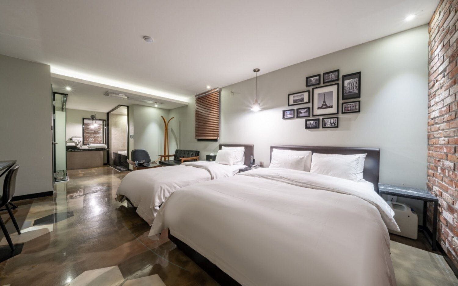 A hotel room with a large bed, a desk, a chair, a mirror, and a brick wall.