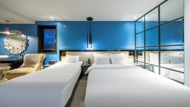 Habitación de hotel con dos camas, un espejo grande y vista al océano.