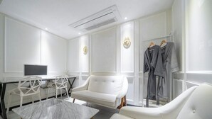 Una habitación moderna con un sofá blanco, una mesita de mármol, un escritorio con un ordenador y un perchero.