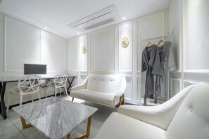 Una habitación moderna con un sofá blanco, una mesita de mármol, un escritorio con un ordenador y un perchero.