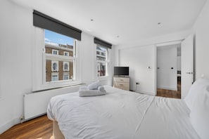 A bedroom with a large bed, a television, and a view of a building through the window. - Stylish London Flat Spr4 (London)