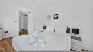 Quarto moderno com uma cama grande, duas mesas de cabeceira, um criado-mudo e uma luminária de parede.