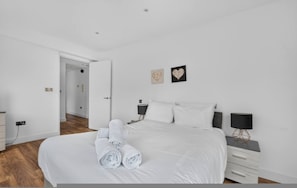 A modern bedroom with a large bed, two bedside tables, a nightstand, and a wall-mounted lamp. - Stylish London Flat Spr4 (London)