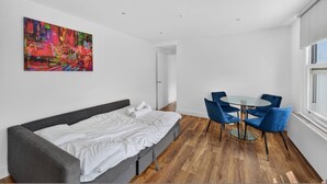Quarto moderno com cama, um quadro, área de refeições com cadeiras e uma janela.